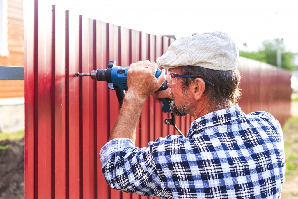 Man with a drill builds metal fence