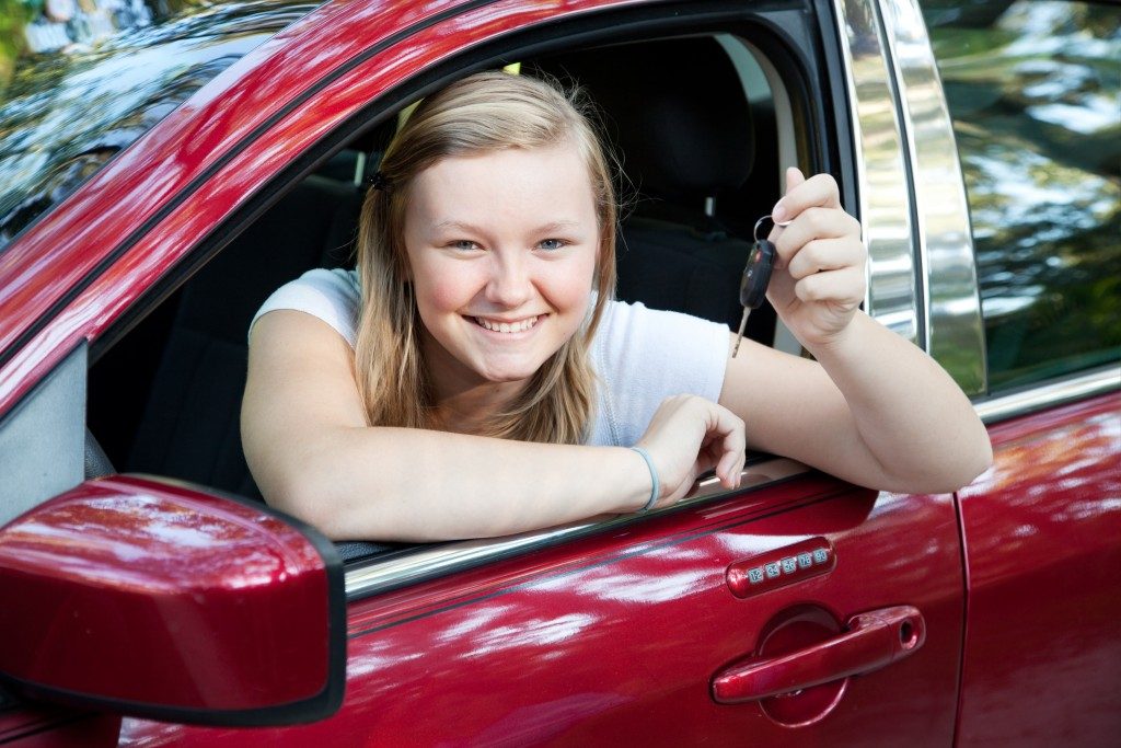 teenage girl sitting in her new car, holding the keys