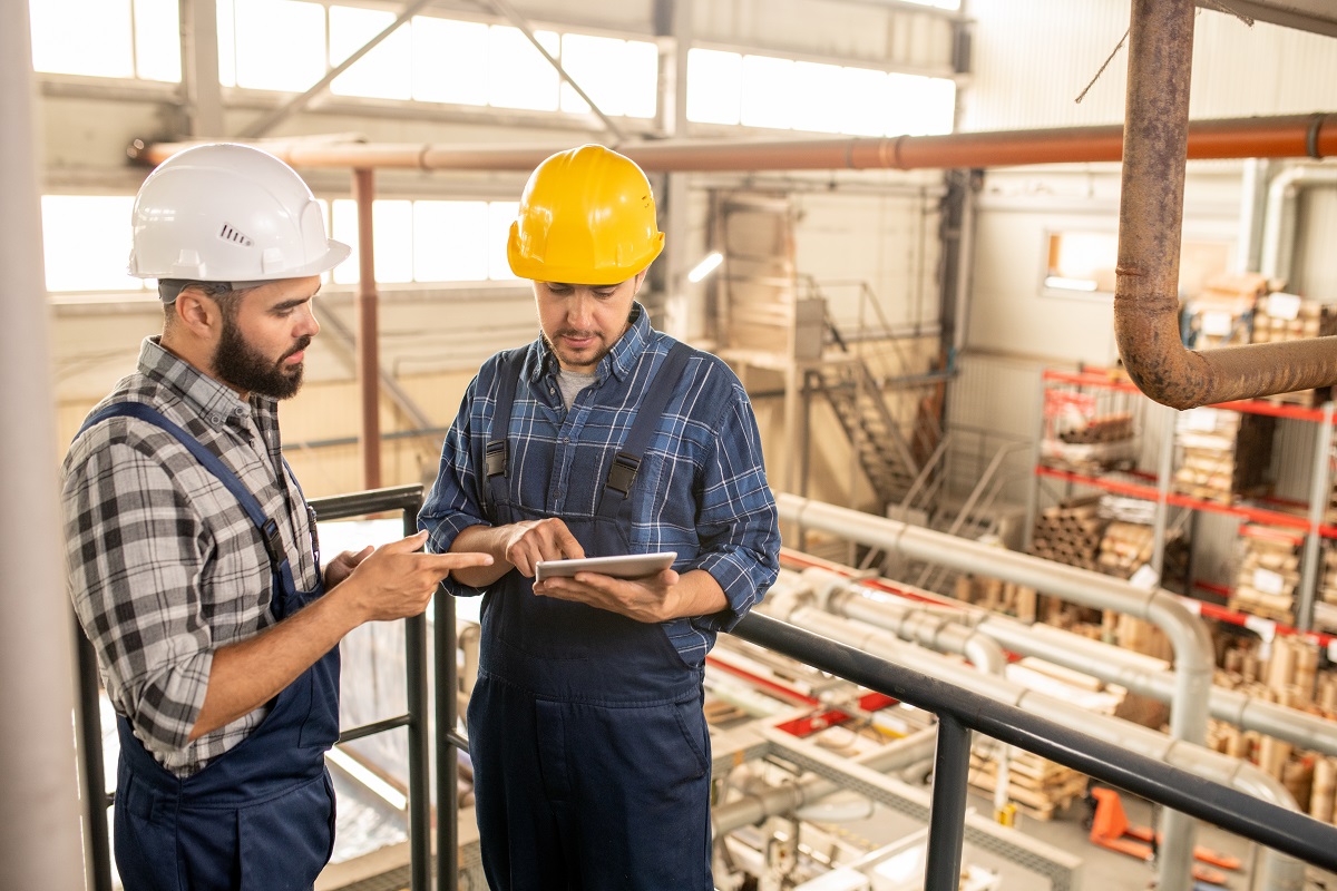 Two young engineers of large factory discussing online technical data