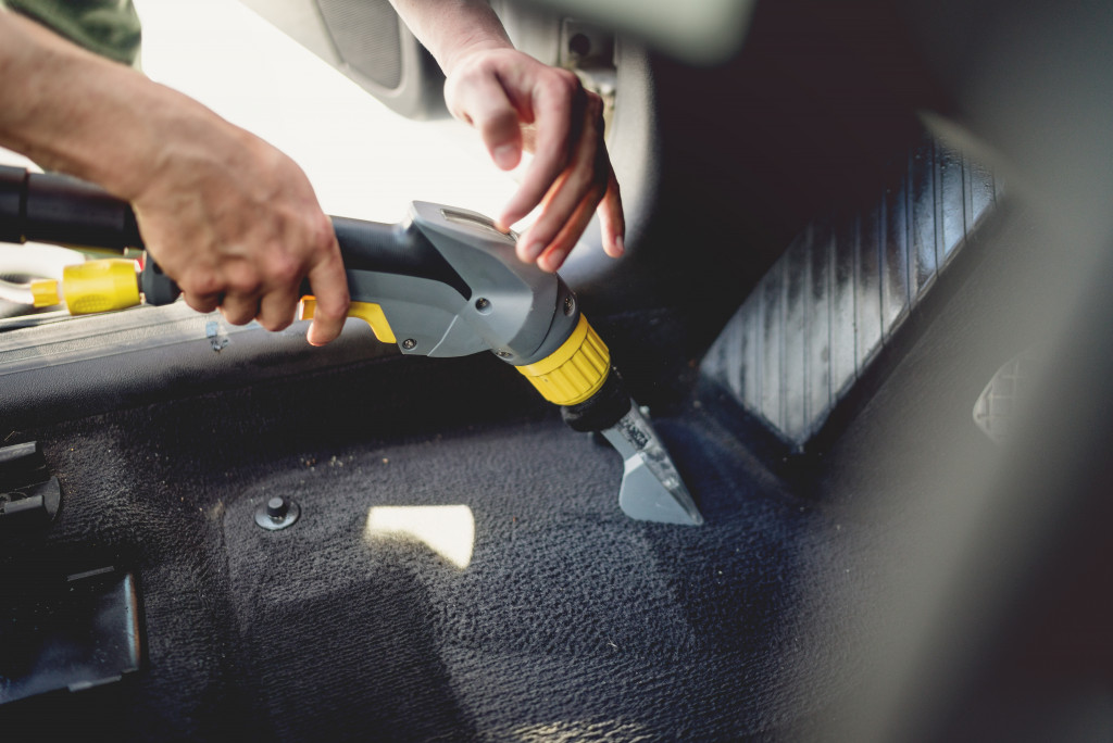 Man cleaning car foot mat with vacuum cleaner 