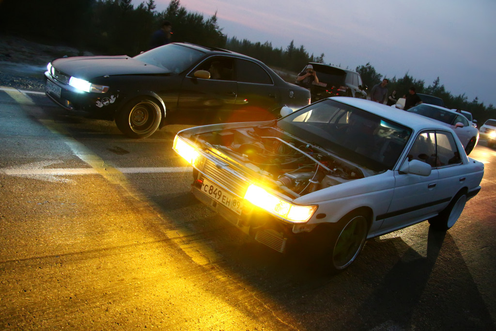 Two cars on the road with open headlights.