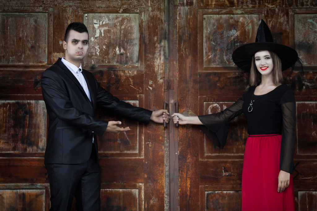 A man and woman dressed as a vampire and a witch opening a door