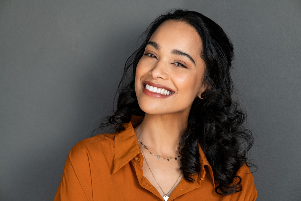 Close up face of young woman with beautiful smile isolated on grey wall