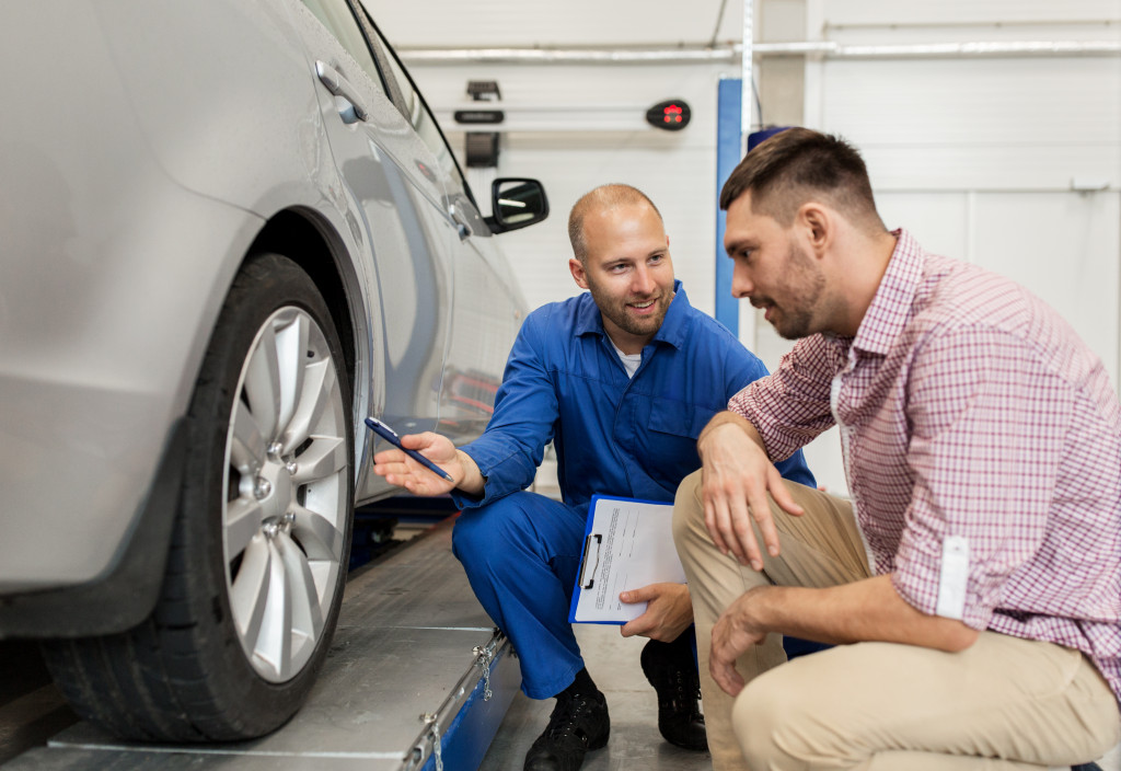  mechanic with clipboard showing tire to man or owner at car shop