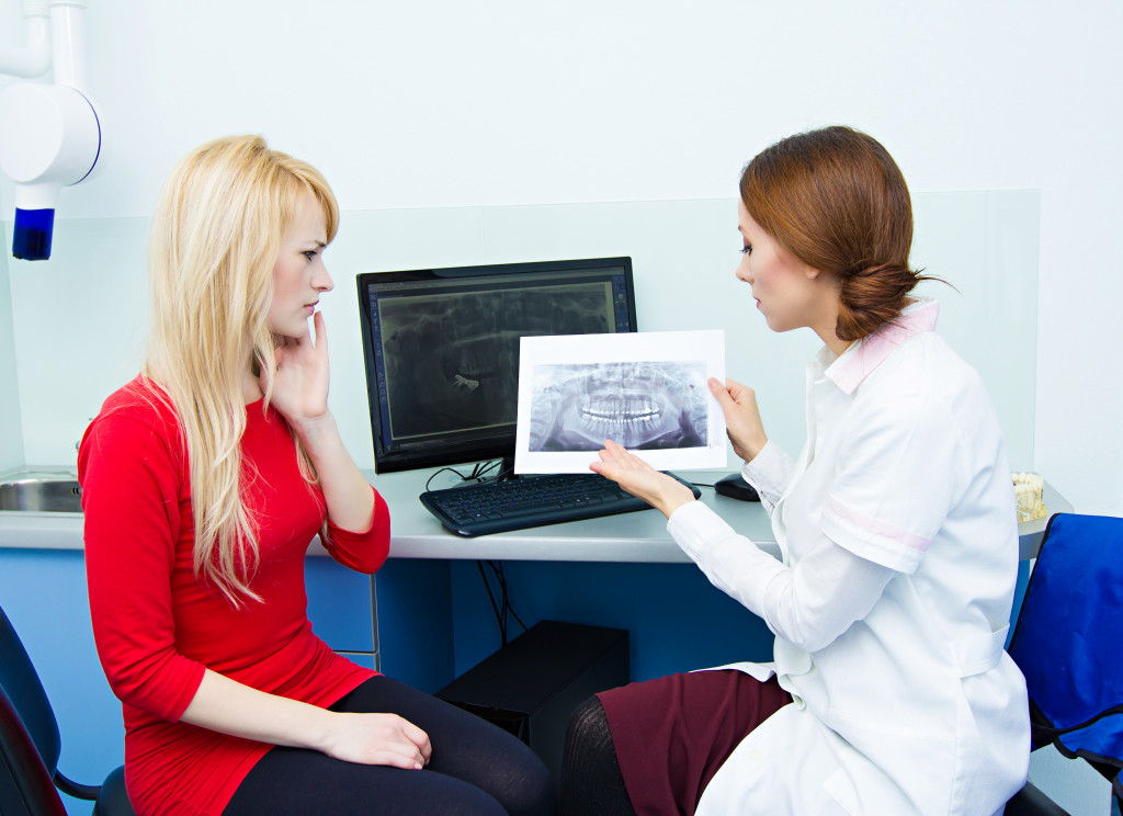 A dentist holds the result of a patient's dental x-ray. Patient looks worried