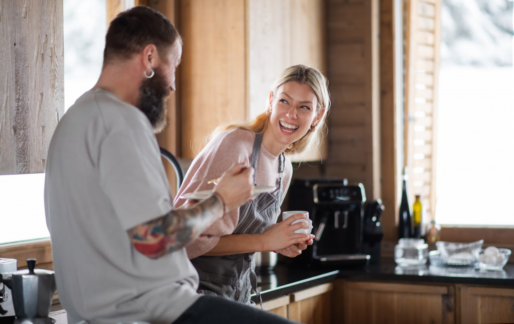 A couple laughing in the kitchen area of a rental apartment while having coffee