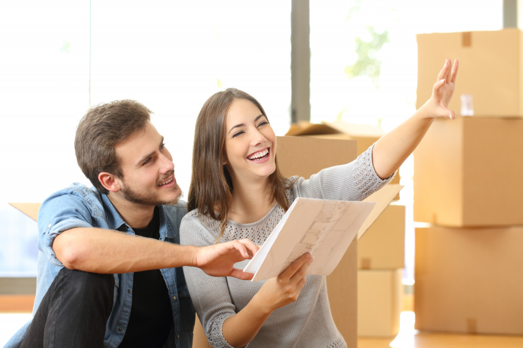 young couple smiling while planning for new home with boxes behind them