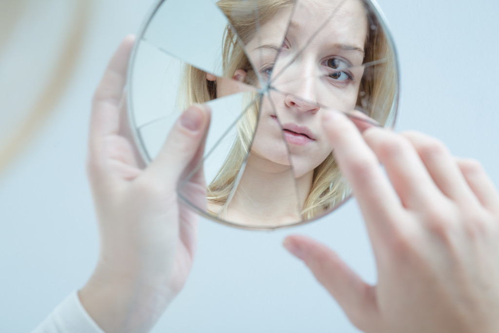 blonde woman looking shyly at broken mirror representing shyness