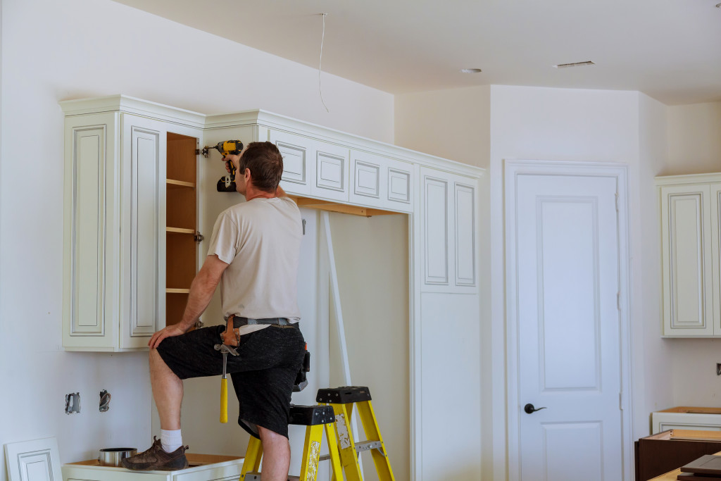 A man up on a counter, fixing the kitchen cabinet