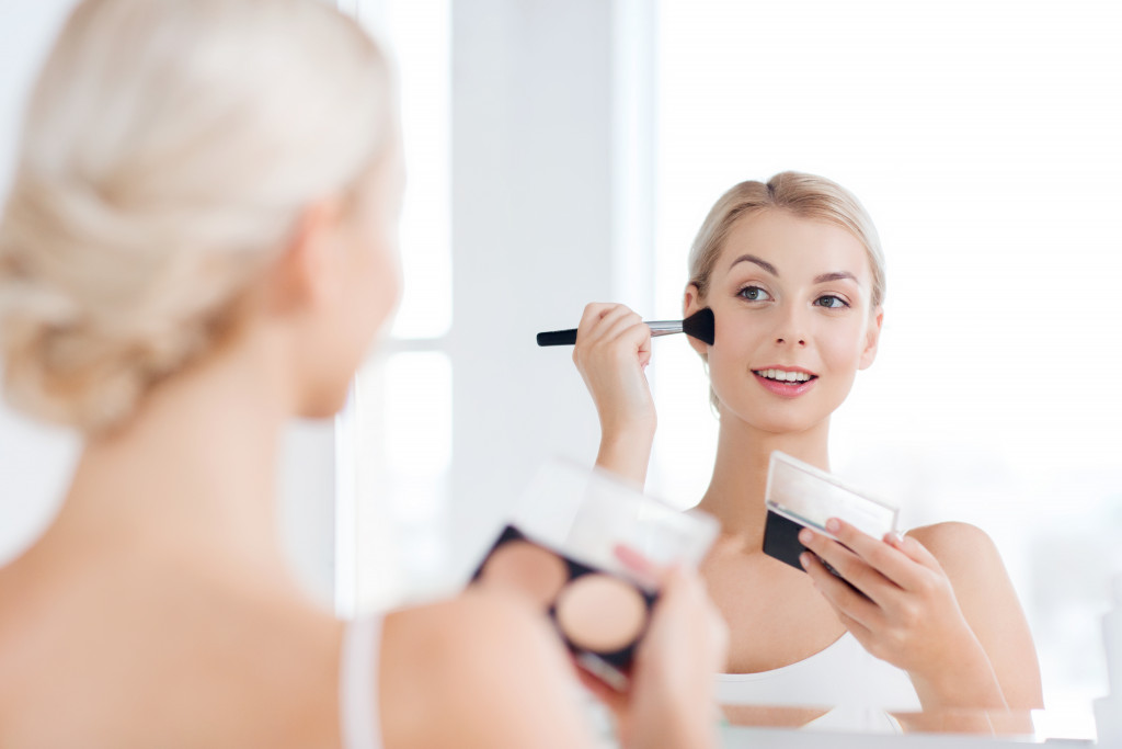 a young woman looking at herself in the mirror applying makeup