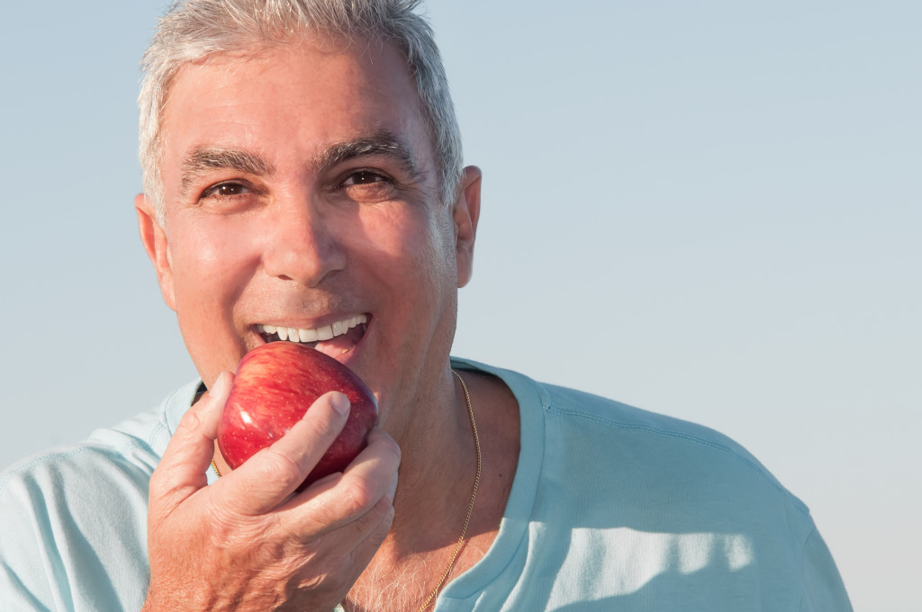 Mature man eating an apple outside.