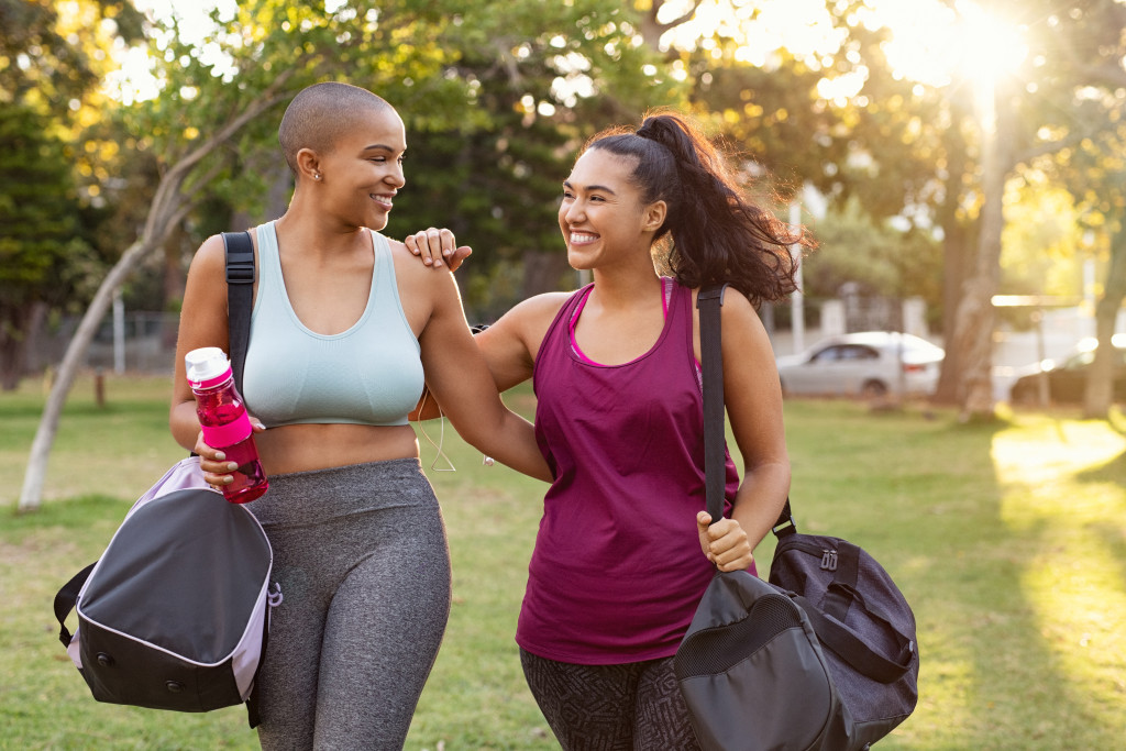 two women laughing after a workout carrying gym bags